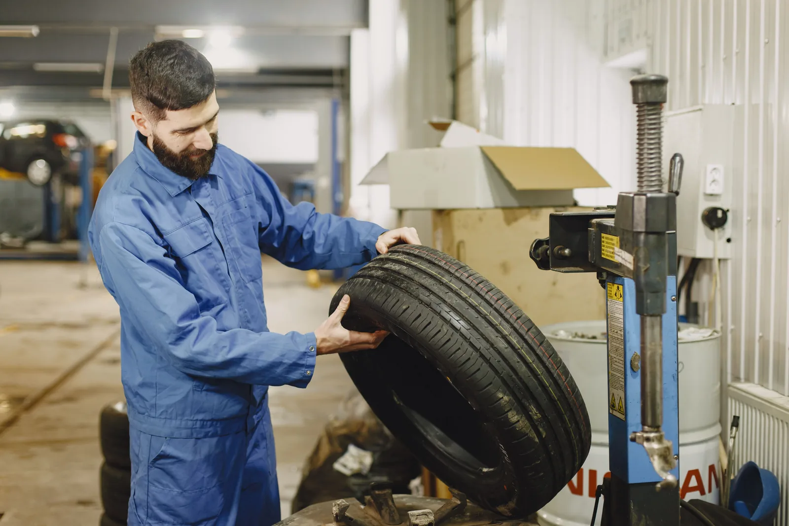 A mechanic examining the tread and sidewall of a car tyre in a workshop